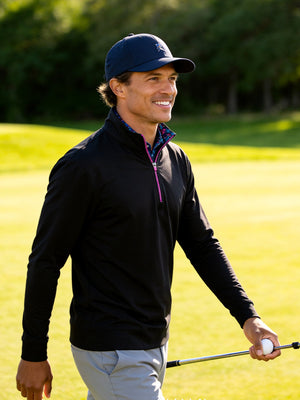 Outdoor shot of a model holding a golf club, wearing the black lightweight golf quarter zip pullover with a relaxed fit