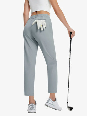 Back lower-body view holding a golf ball with glove in rear pocket wearing LIGHT GREY Women's 7/8 Ankle Golf Track Pants.