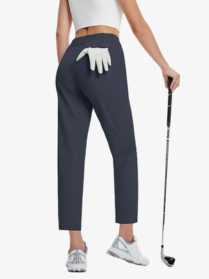 Back lower-body view holding a golf ball with glove in rear pocket wearing NAVY Women's 7/8 Ankle Golf Track Pants.