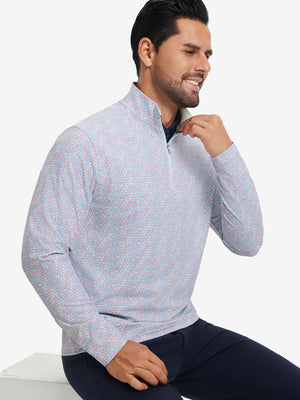 Model seated on chair, wearing full print quarter zip pullover in colorful hexagon, casual upper body view.