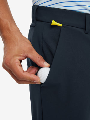 Hand placing a golf ball into pocket of water-resistant golf stretch nylon pants in navy.